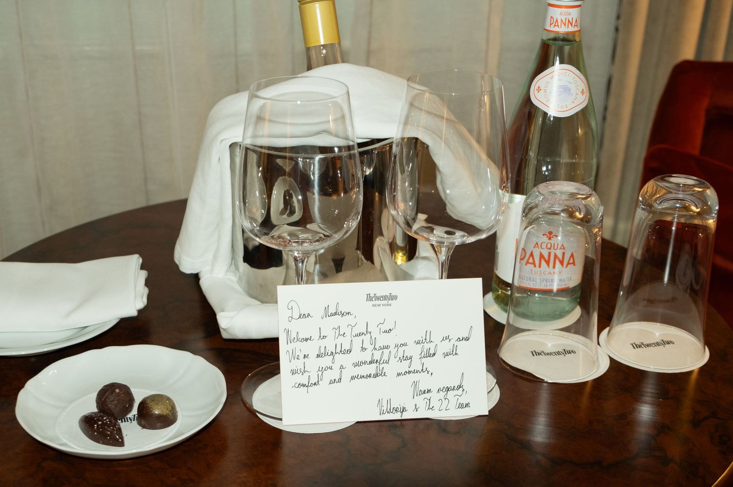 Hotel welcome amenity with wine bottle in ice bucket, Acqua Panna water, chocolates, and personalized note.