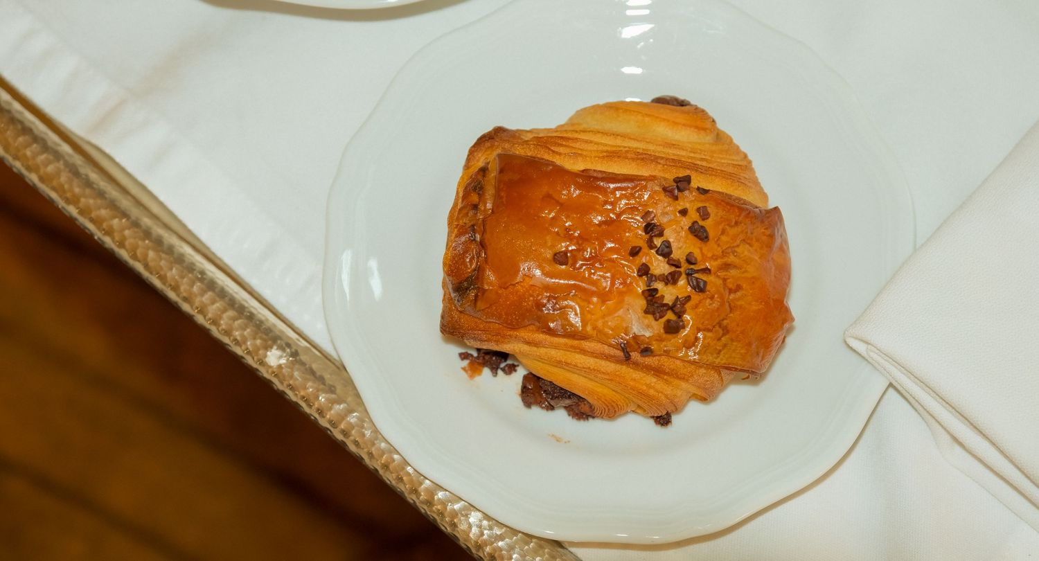 Golden baked pain au chocolat with chocolate pieces on elegant white plate on decorative tray.