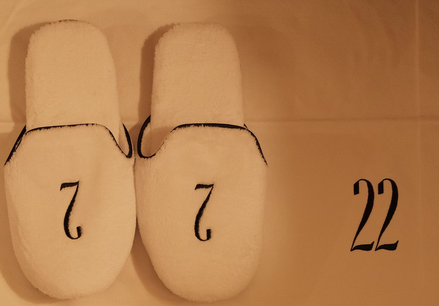 White hotel slippers with number 7 embroidered on each, next to The Twenty Two logo.