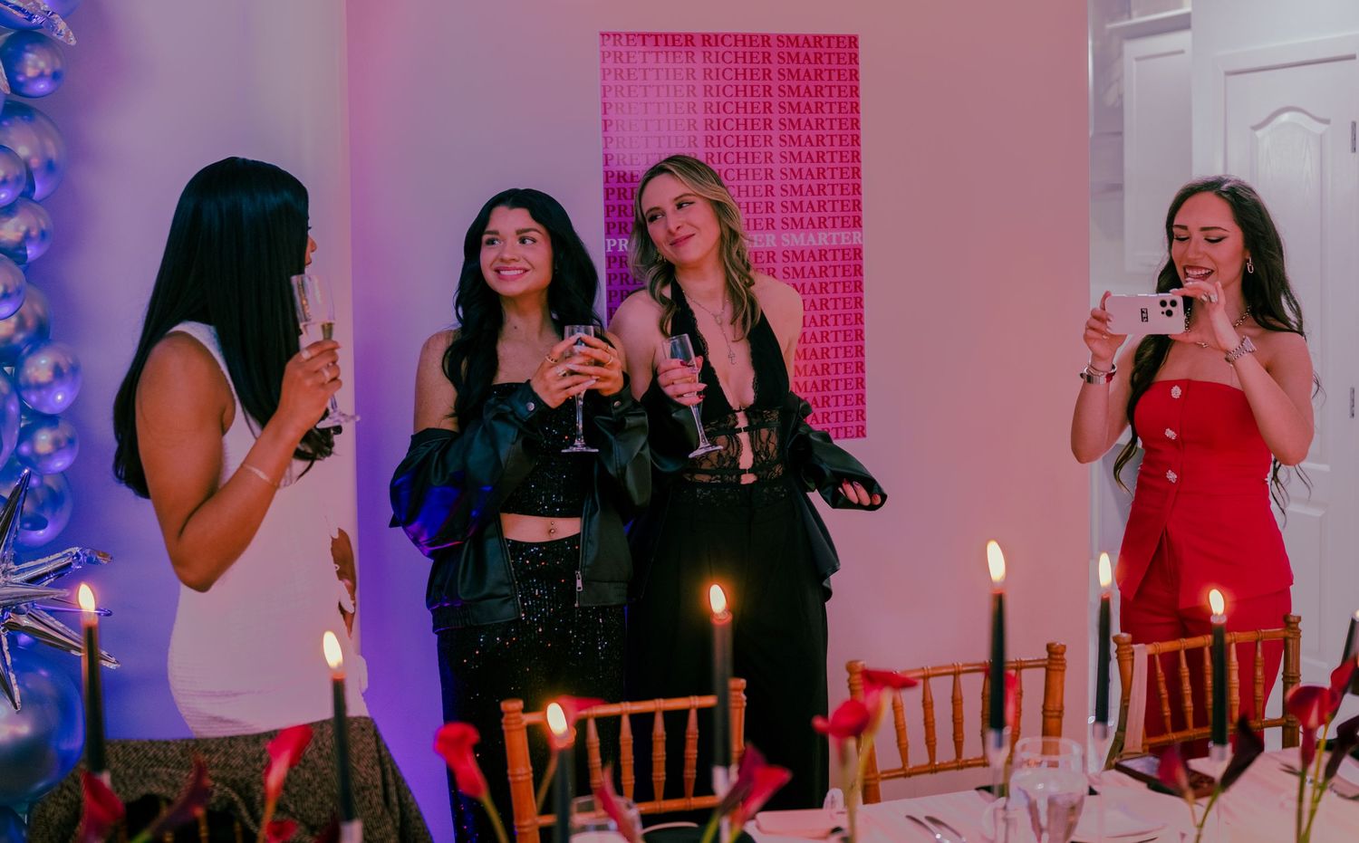 Four women toasting with champagne glasses at a candlelit dinner party with festive decorations.
