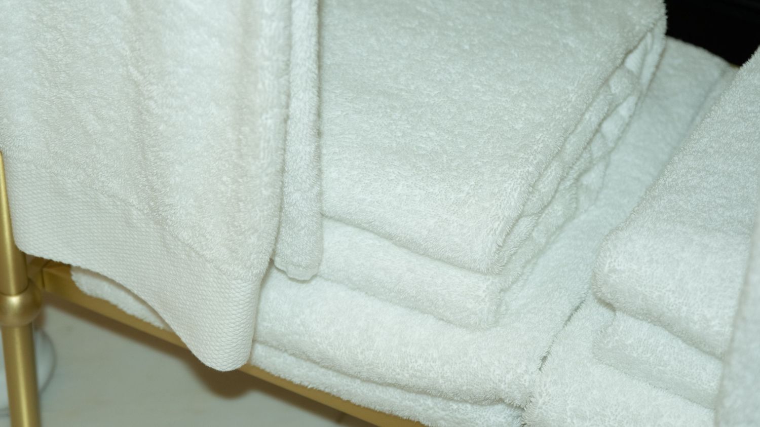 Neatly folded white hotel towels stacked on a gold towel rack.