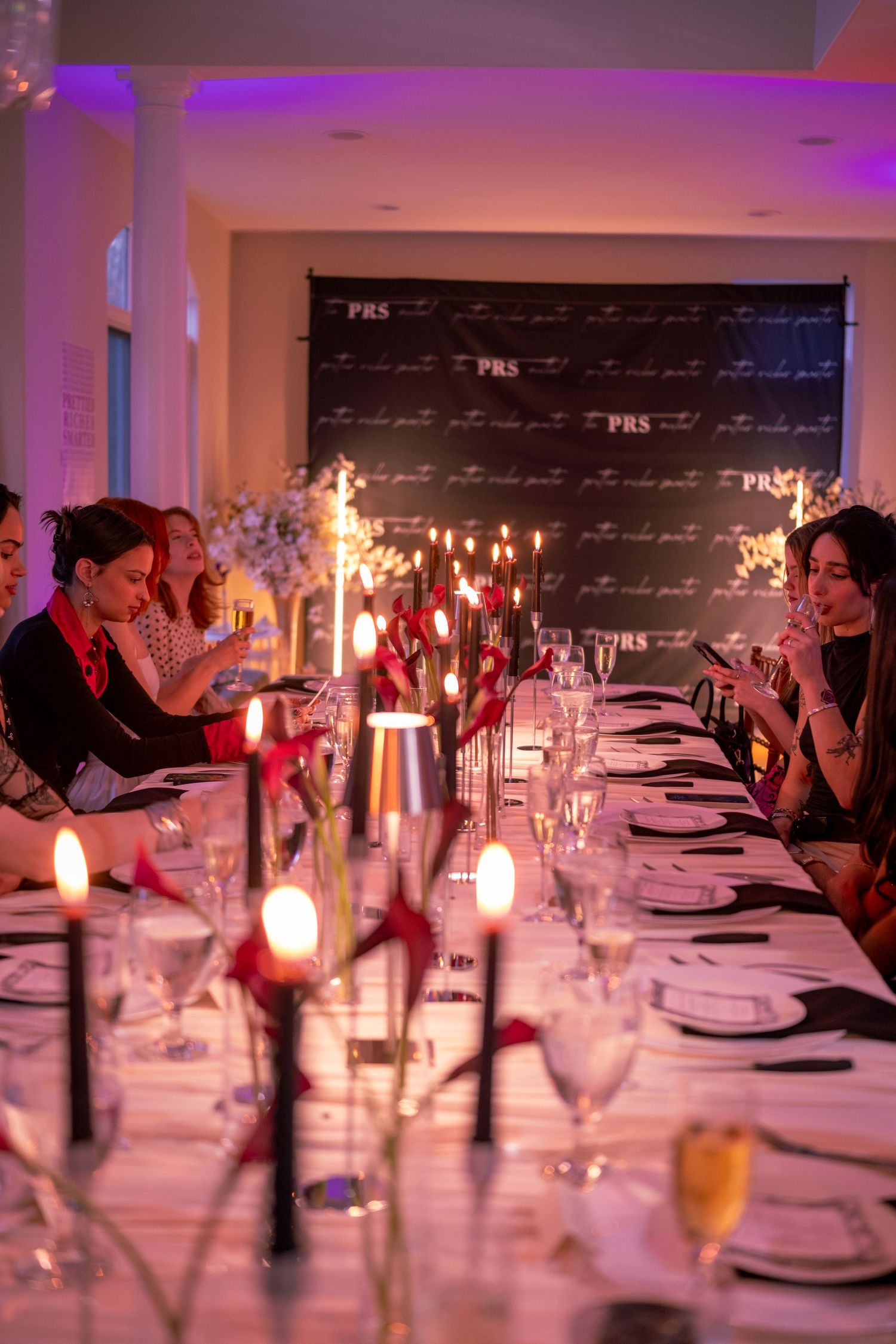 Guests seated at a long elegantly set dinner table at a PRS branded event with purple ambient lighting.