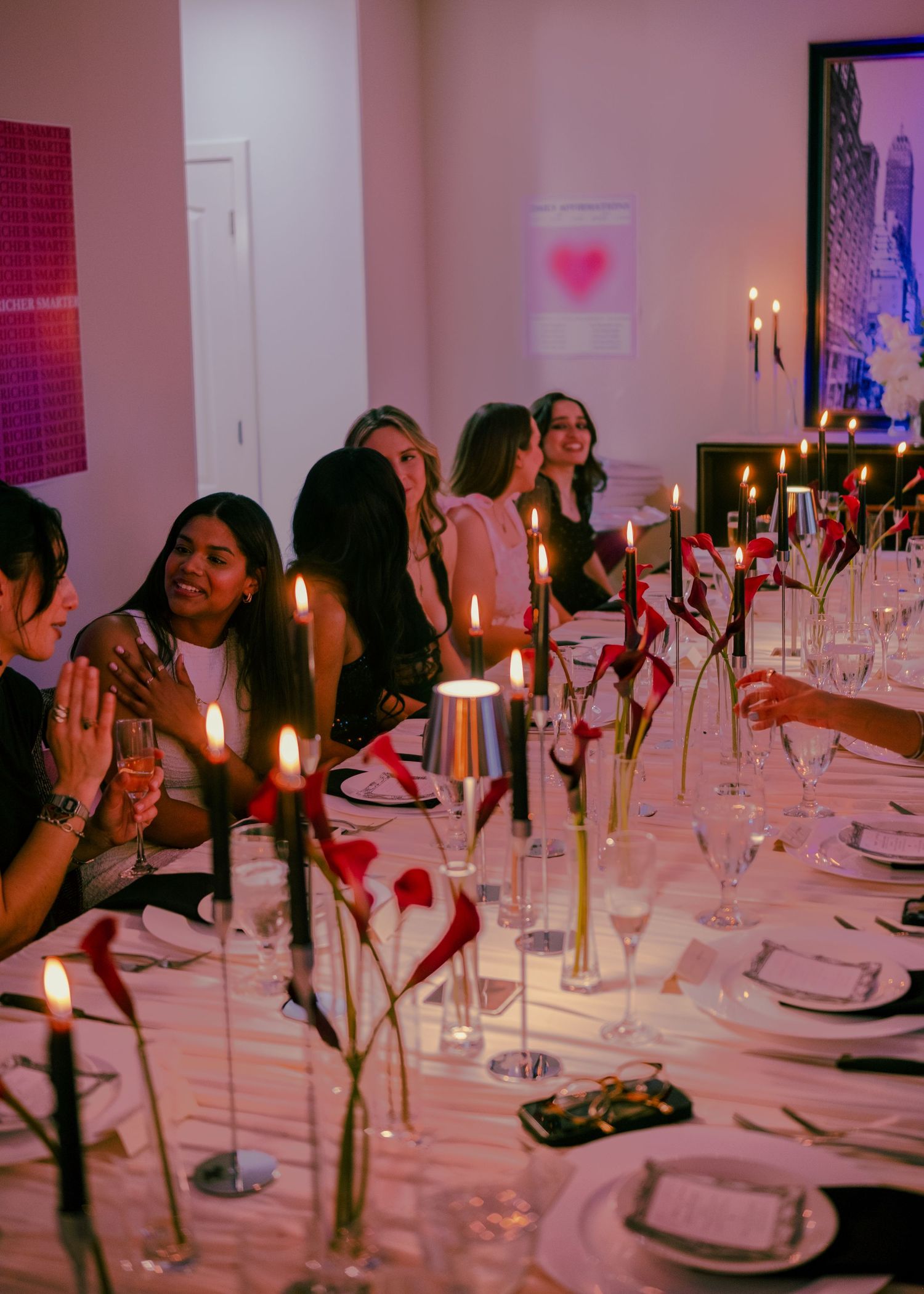 Women seated at an elegantly decorated dinner table with candles and red floral arrangements at a PRS event.