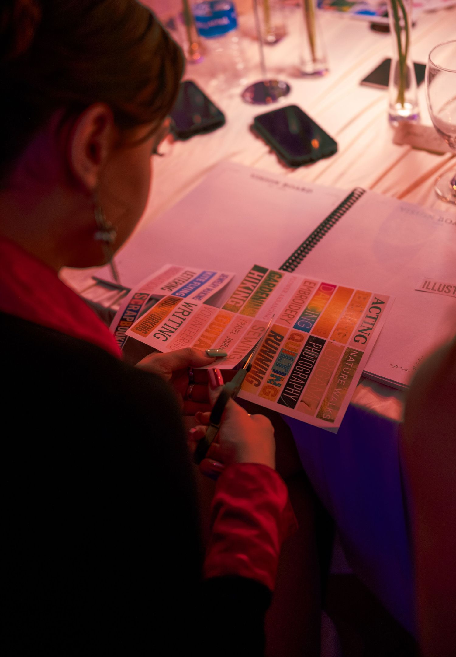 Woman reviewing colorful sticker charts in a spiral notebook at a candlelit event dinner table.