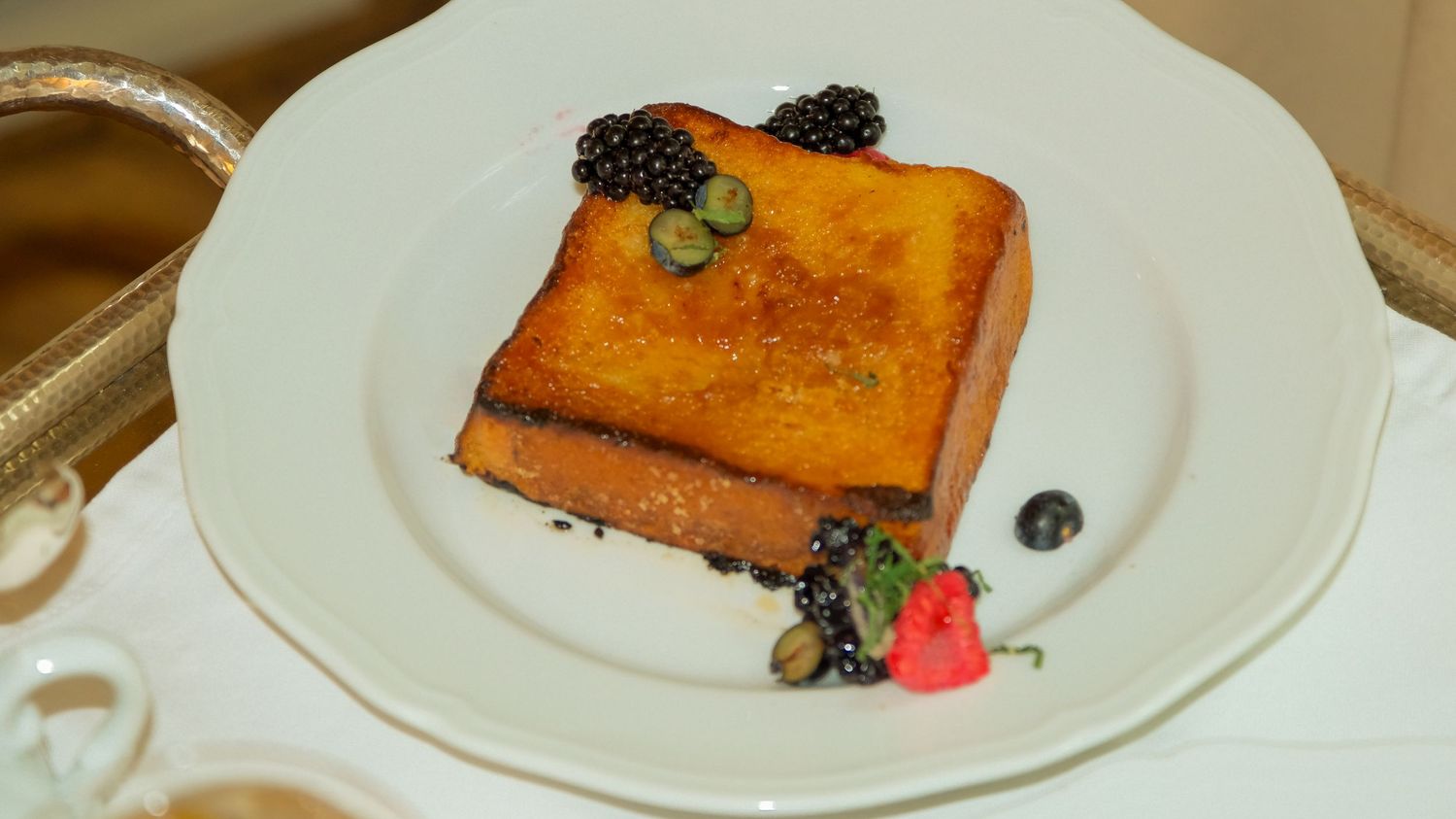 Golden French toast topped with fresh blackberries, blueberries, and strawberry on a white ceramic plate.