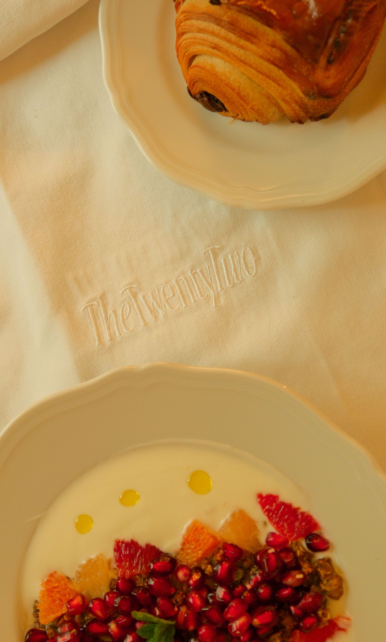 The Twenty Two restaurant table setting with pomegranate dessert plate and croissant on embroidered linen napkin.