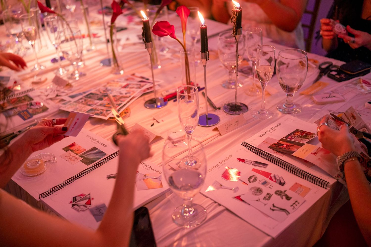Overhead view of candlelit dinner table with scattered papers, wine glasses, and floral decorations.