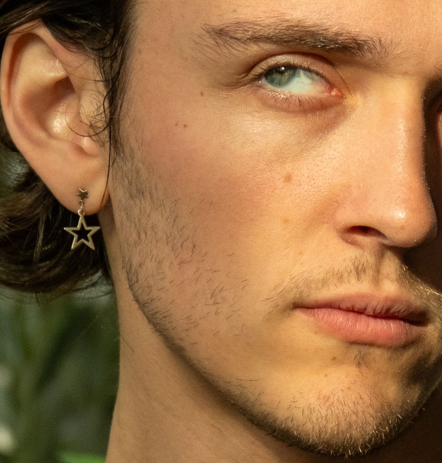 Close-up of young man with light eyes wearing a star-shaped gold hoop earring.
