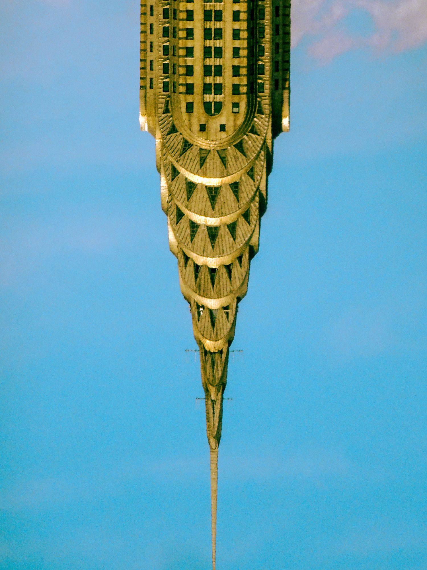 Inverted view of the Chrysler Building's Art Deco spire against a clear blue sky in New York City.