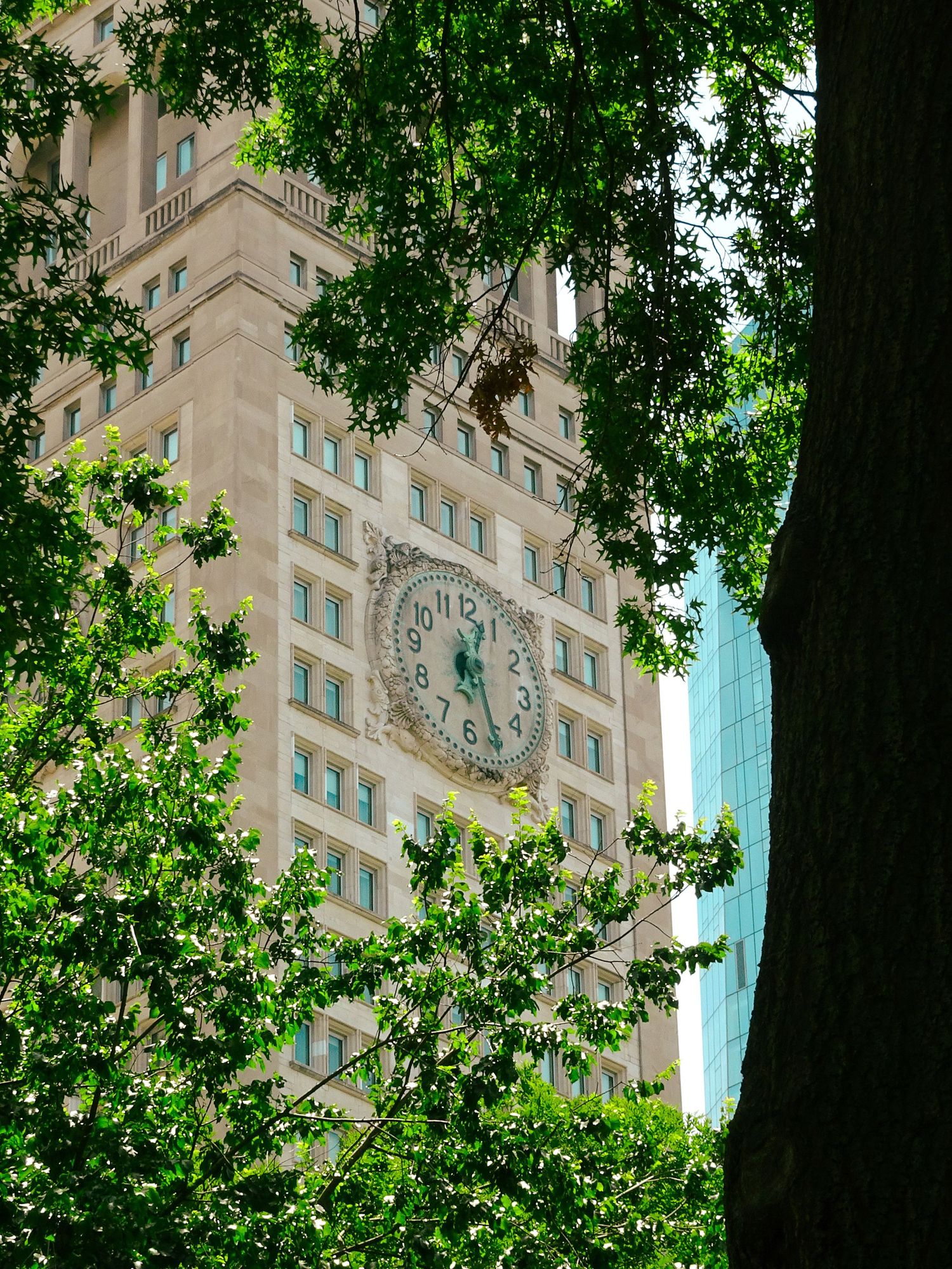 Historic building with ornate clock tower framed by lush green trees in an urban setting.