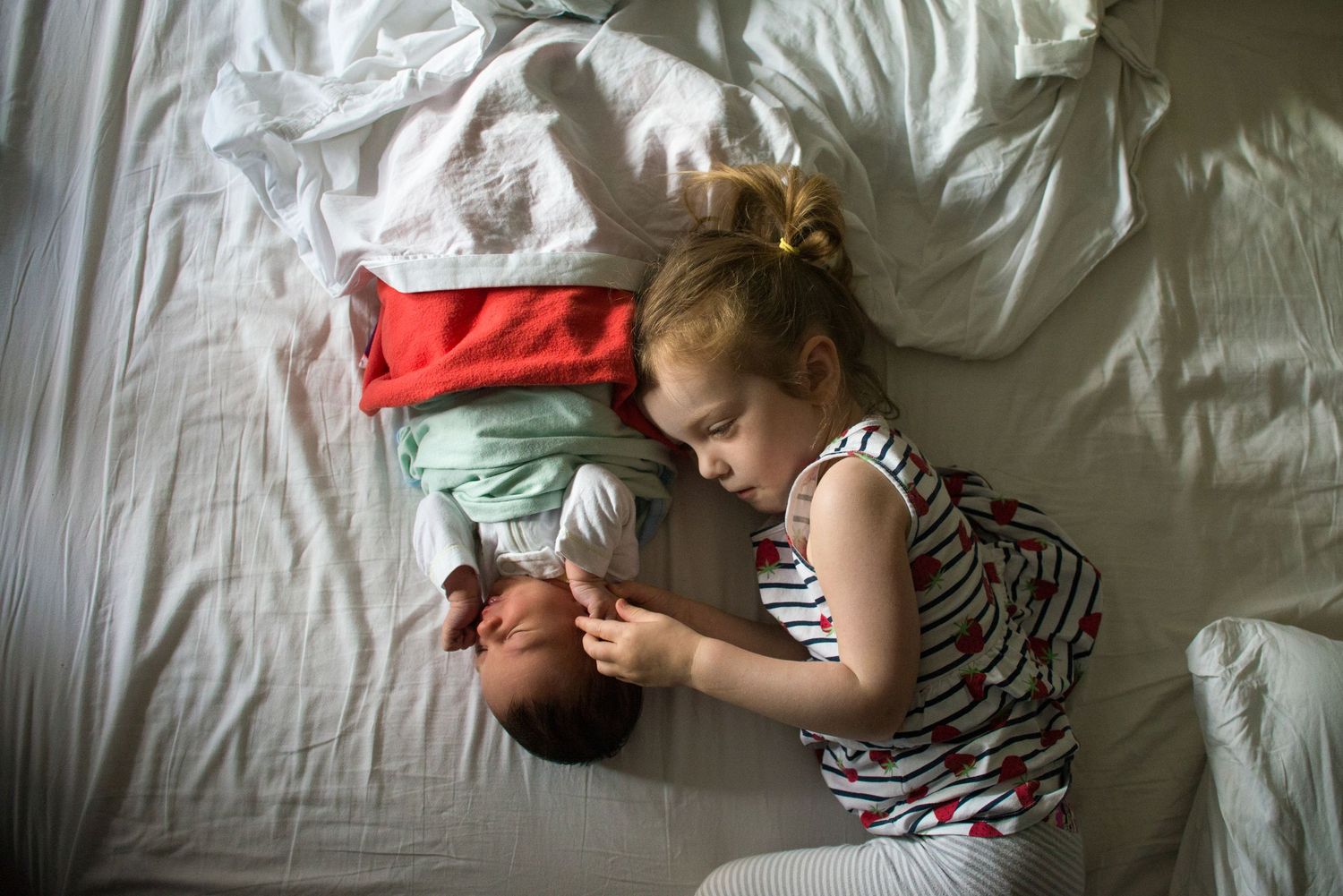 A young child in a striped dress lies on white bedding next to folded clothes.