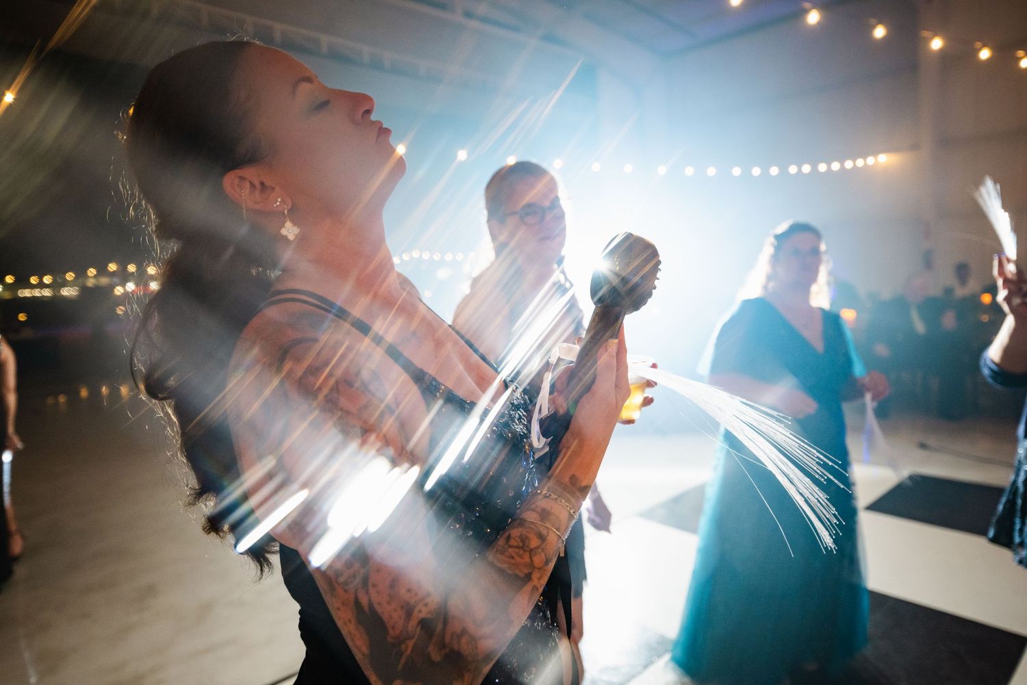Tattooed woman dancing joyfully with sparklers on checkered dance floor at wedding reception.