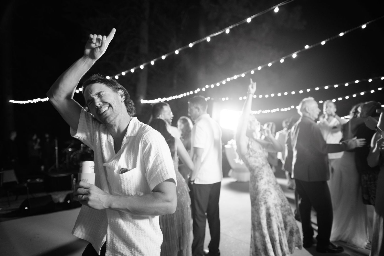 String lights glow above a dance floor as guests celebrate at an evening reception.