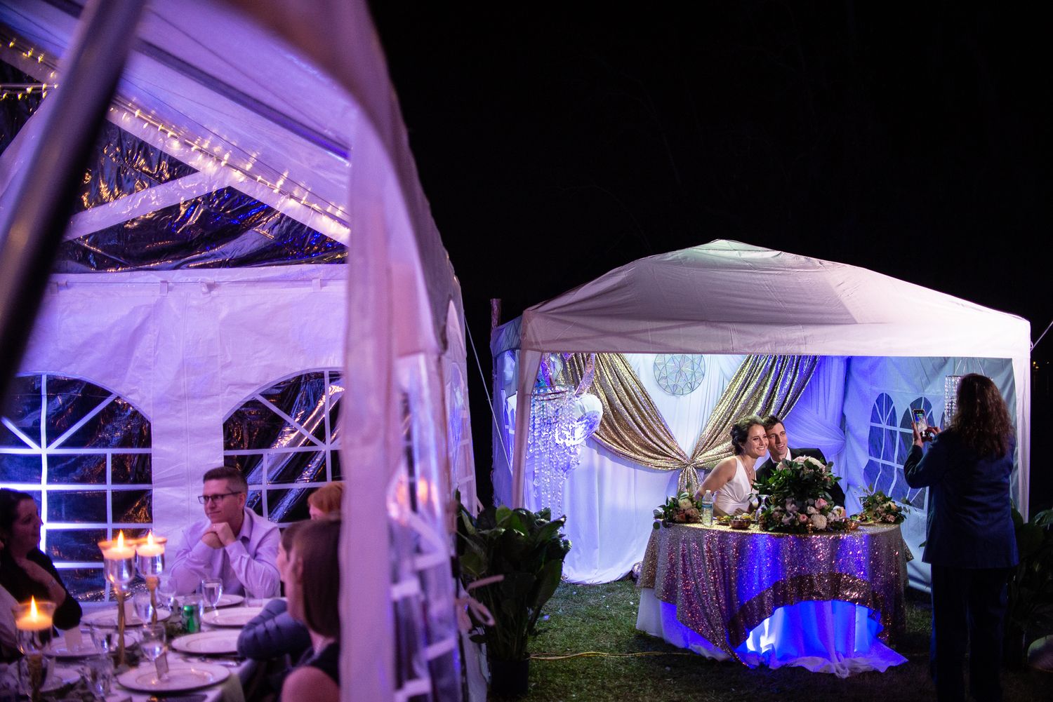 Elegant wedding reception tent setup with purple uplighting and white draping creating a romantic atmosphere.