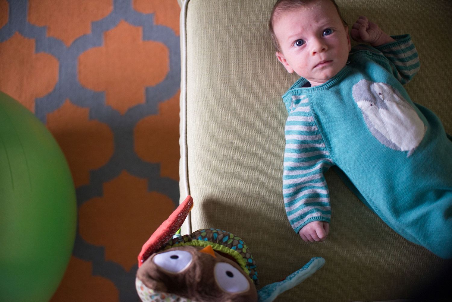 A baby rests on a beige couch against an orange patterned wallpaper background.