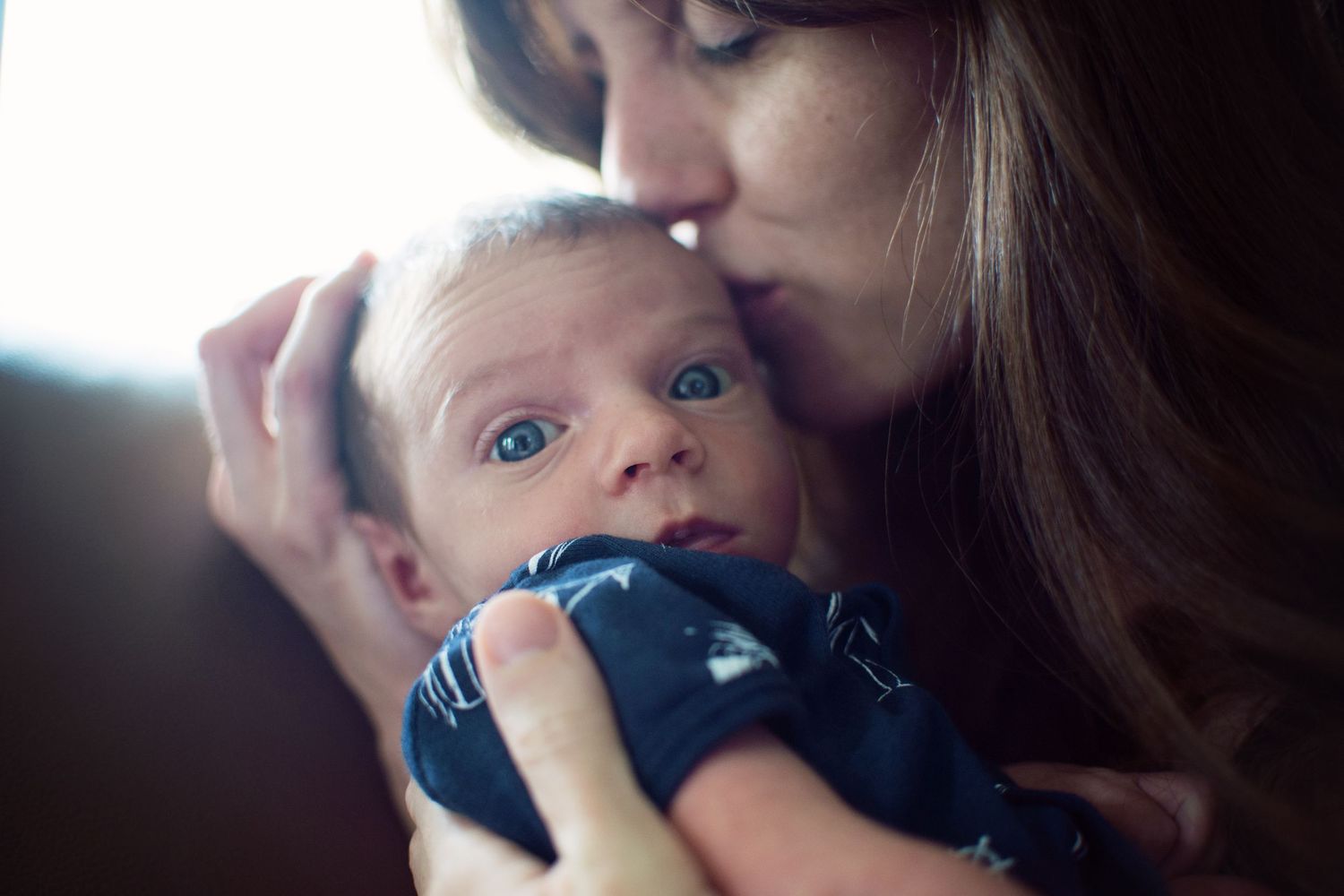 Baby with blue eyes resting on a soft surface while being comforted.