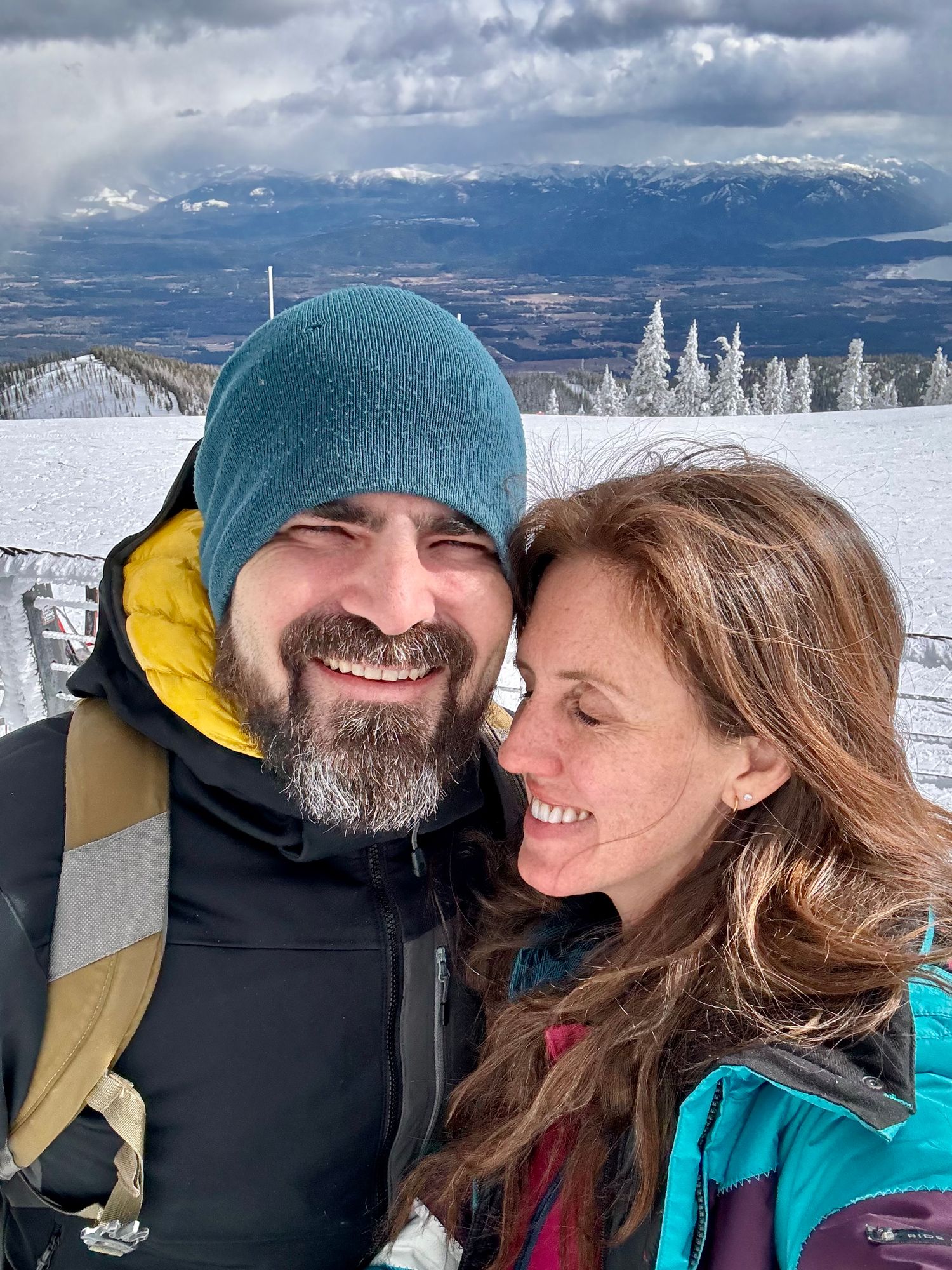 Winter sports enthusiasts sharing a close moment against snowy mountain backdrop.