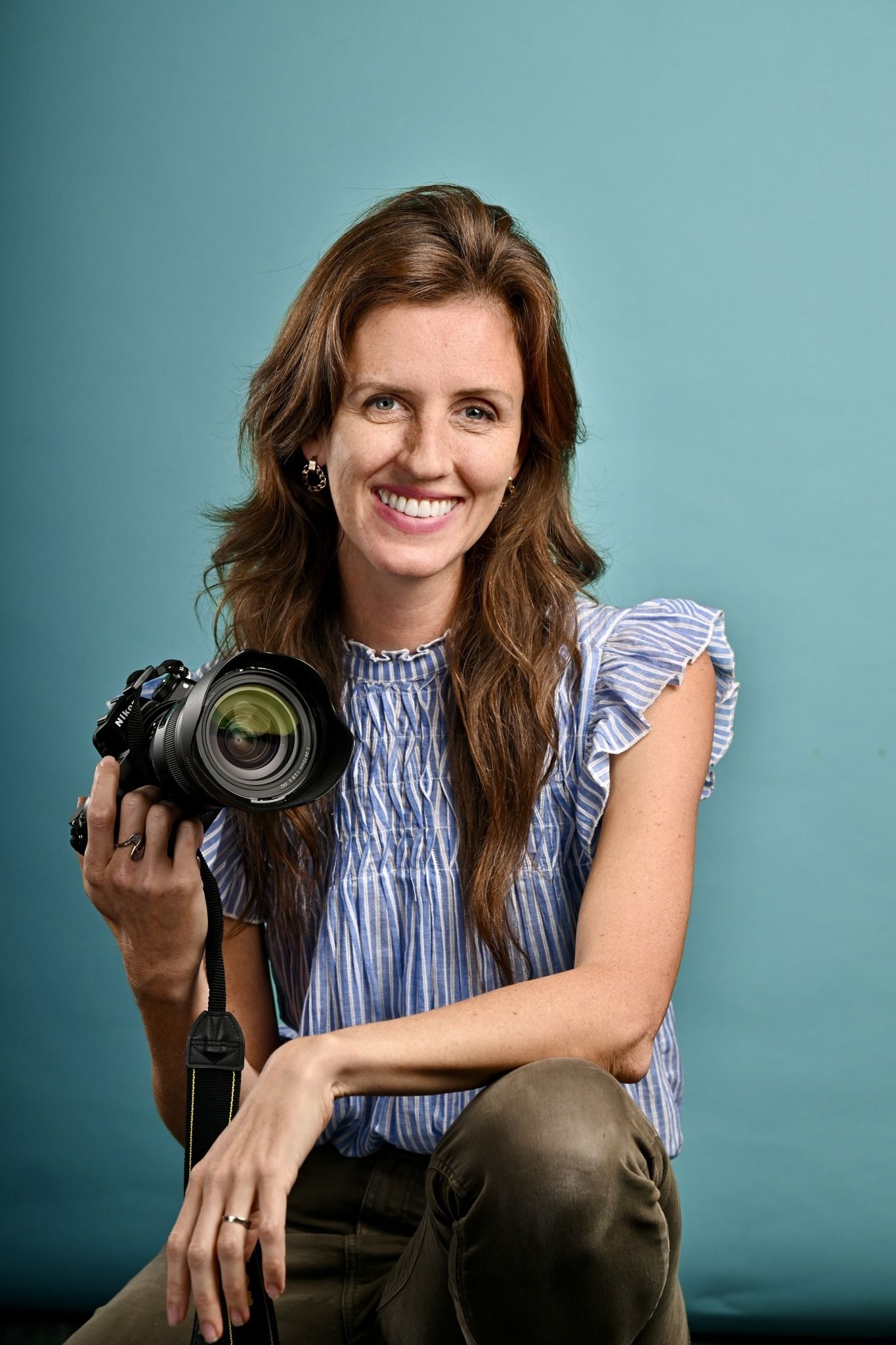 A photographer displays camera equipment against a turquoise studio backdrop.