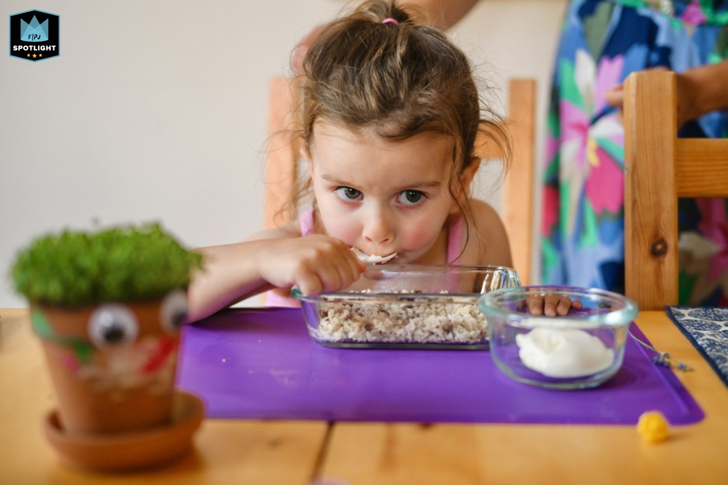 A person peeks over the edge of a table at a glass jar while crafting or doing a creative activity.