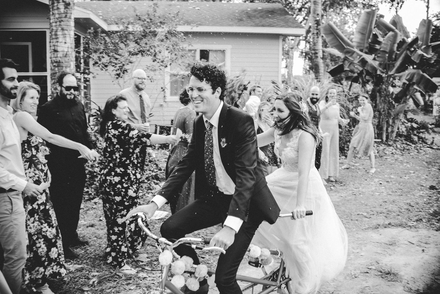 A joyful couple jumps together during an outdoor garden wedding celebration captured in black and white photography.