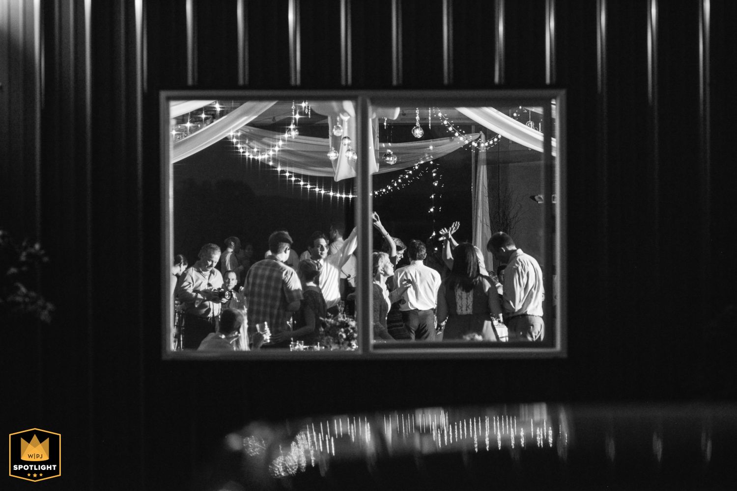Musicians perform in a carousel shelter captured in a dramatic black and white photograph through a framed window.