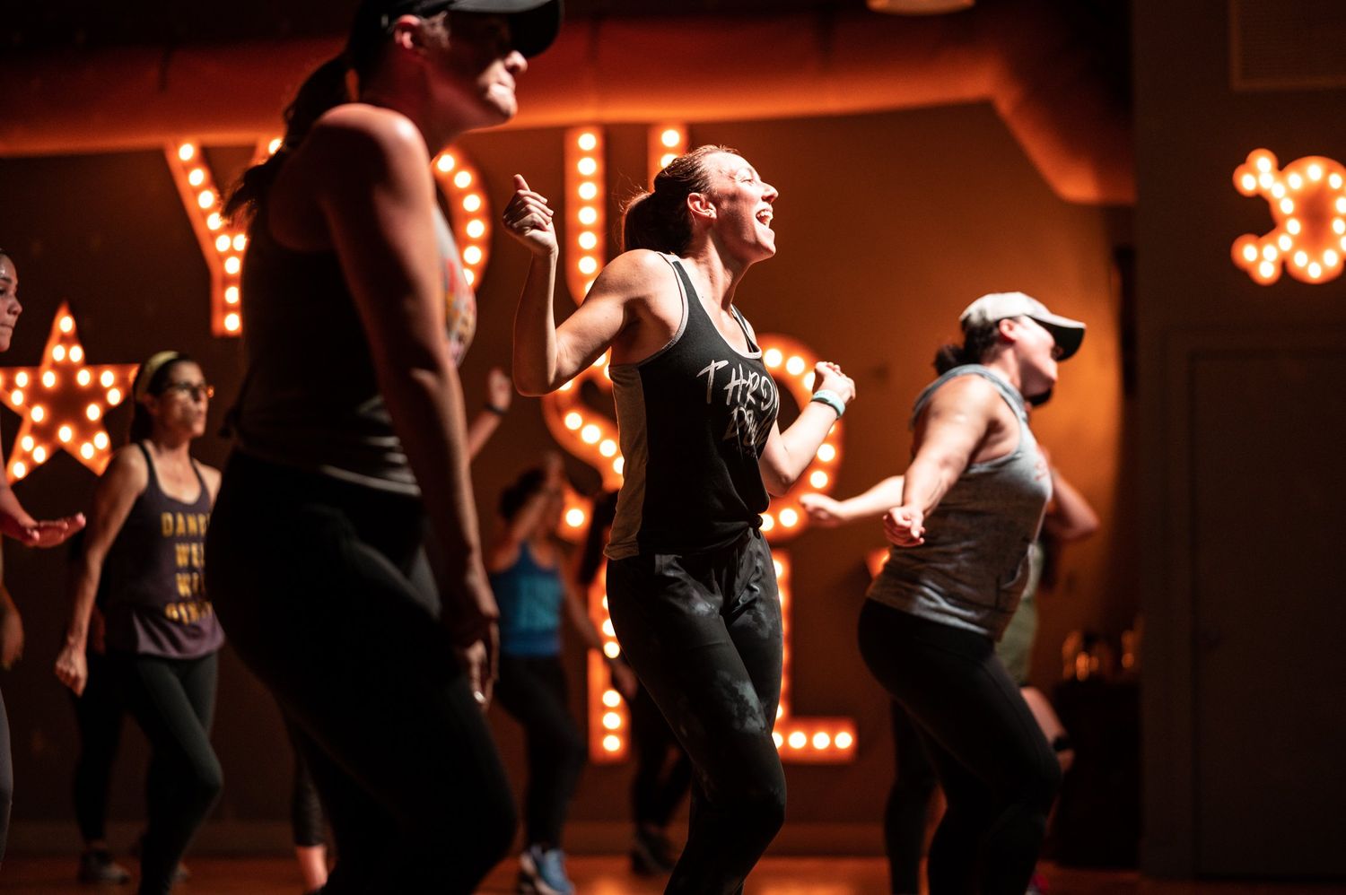 Group of dancers practicing synchronized movements in a dimly lit studio with warm lighting.