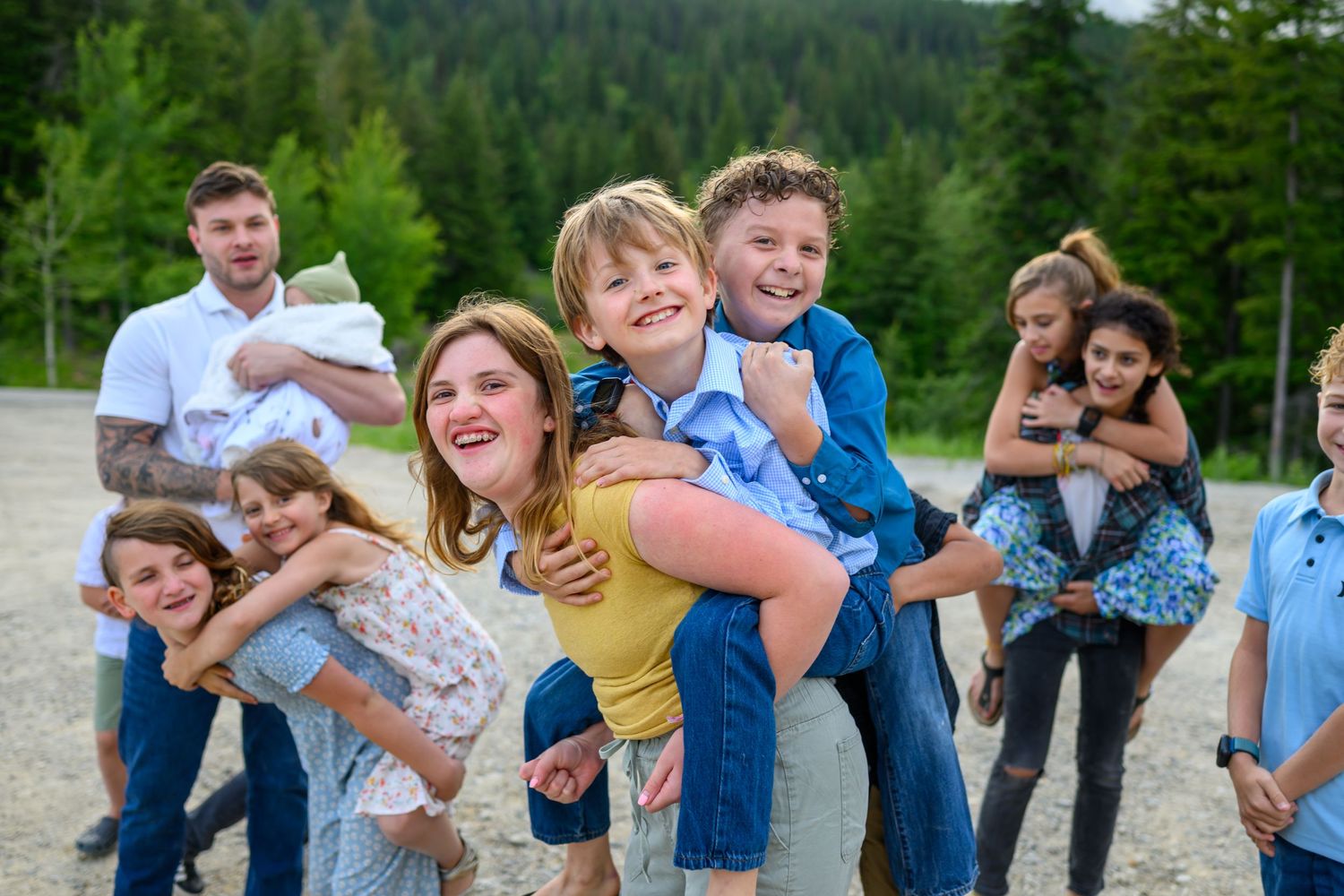 A joyful family with children playing piggyback rides outdoors near a forest, smiling and laughing together.