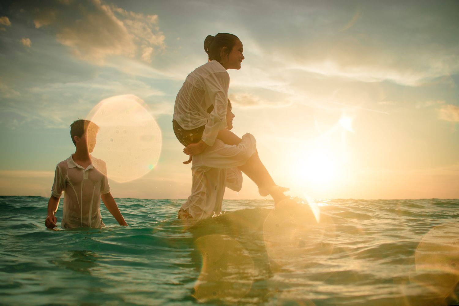 A couple splashes playfully in the ocean water during a golden sunset creating a dreamy romantic atmosphere.