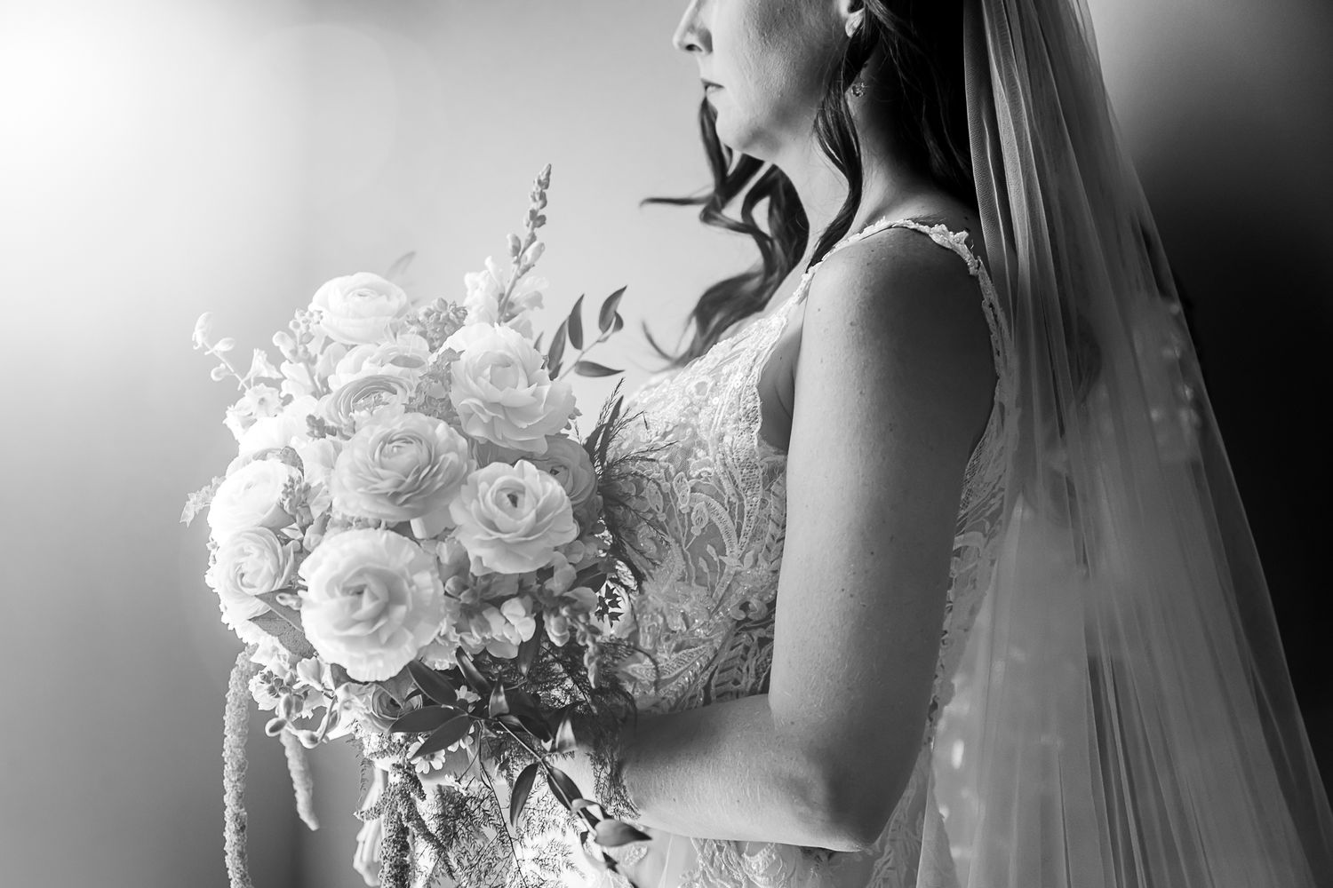 Elegant black and white side profile of a bride holding a luxurious bouquet of white roses and flowers.