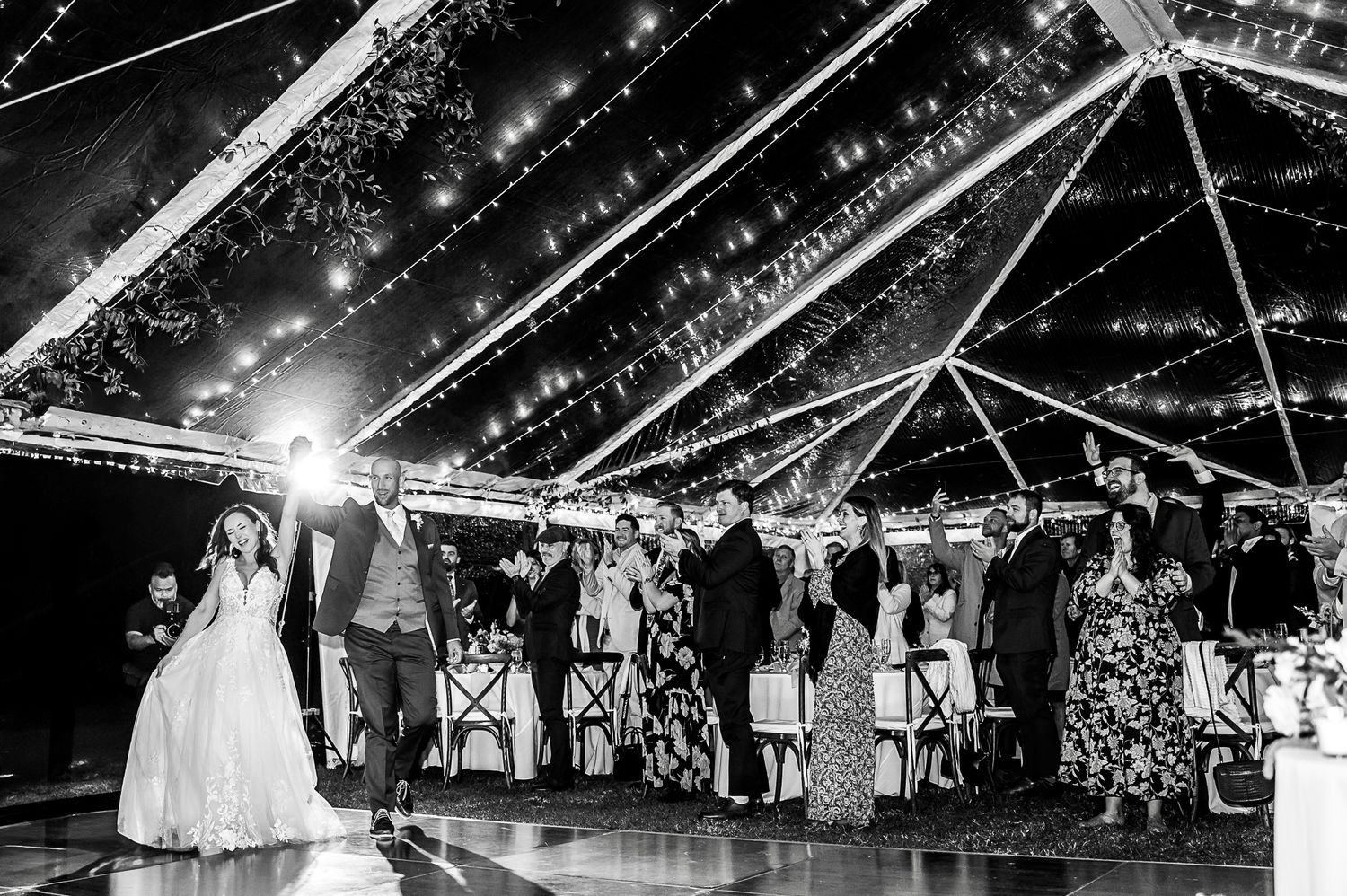 Wedding reception celebration under a clear tent with string lights and guests dancing on the dance floor.