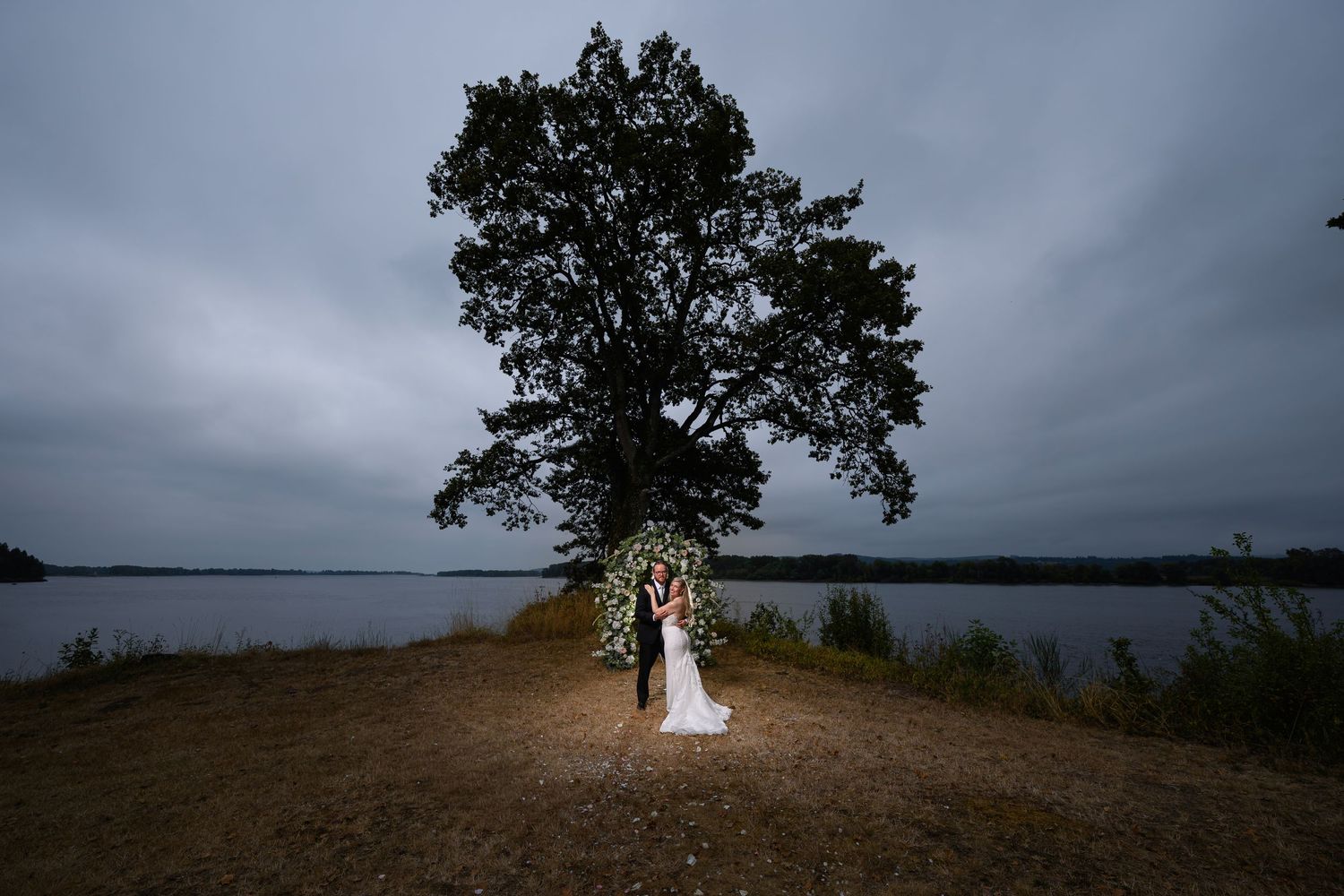 Dramatic stormy skies create a moody backdrop for a lone tree silhouetted against a dark horizon.