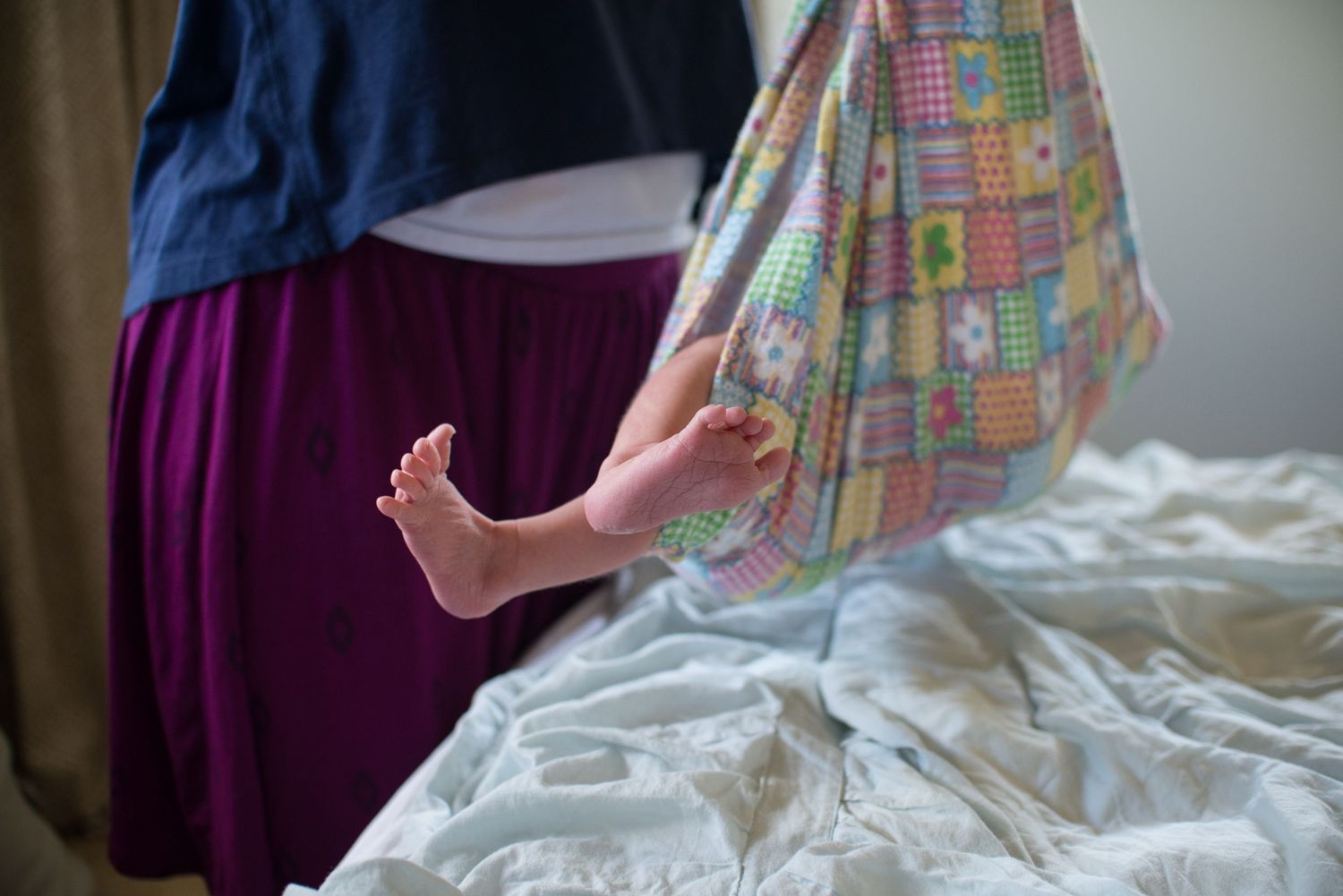 A colorful patchwork quilt with pastel patterns lies on a white bed.