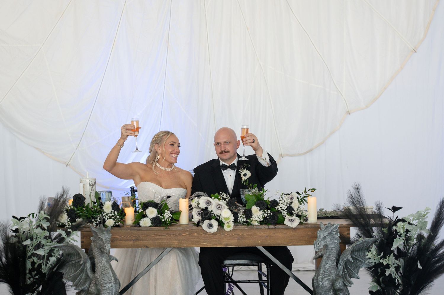 Bride and groom raise champagne glasses in a toast at their elegant floral sweetheart table.
