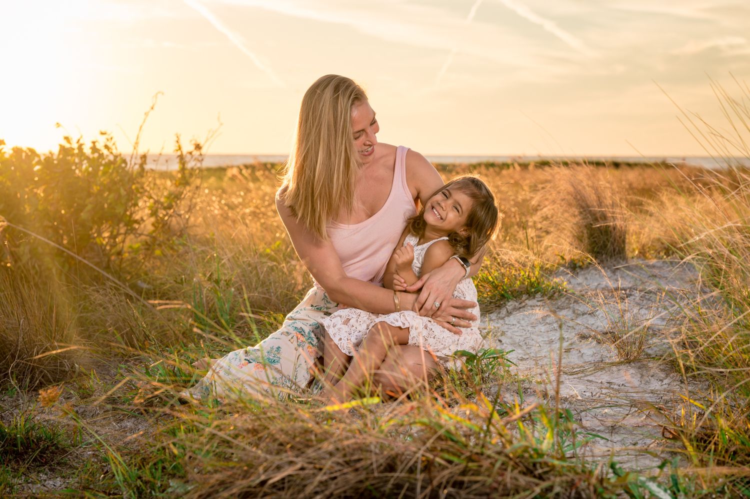 Mother and daughter embracing in golden sunset light in a grassy field.