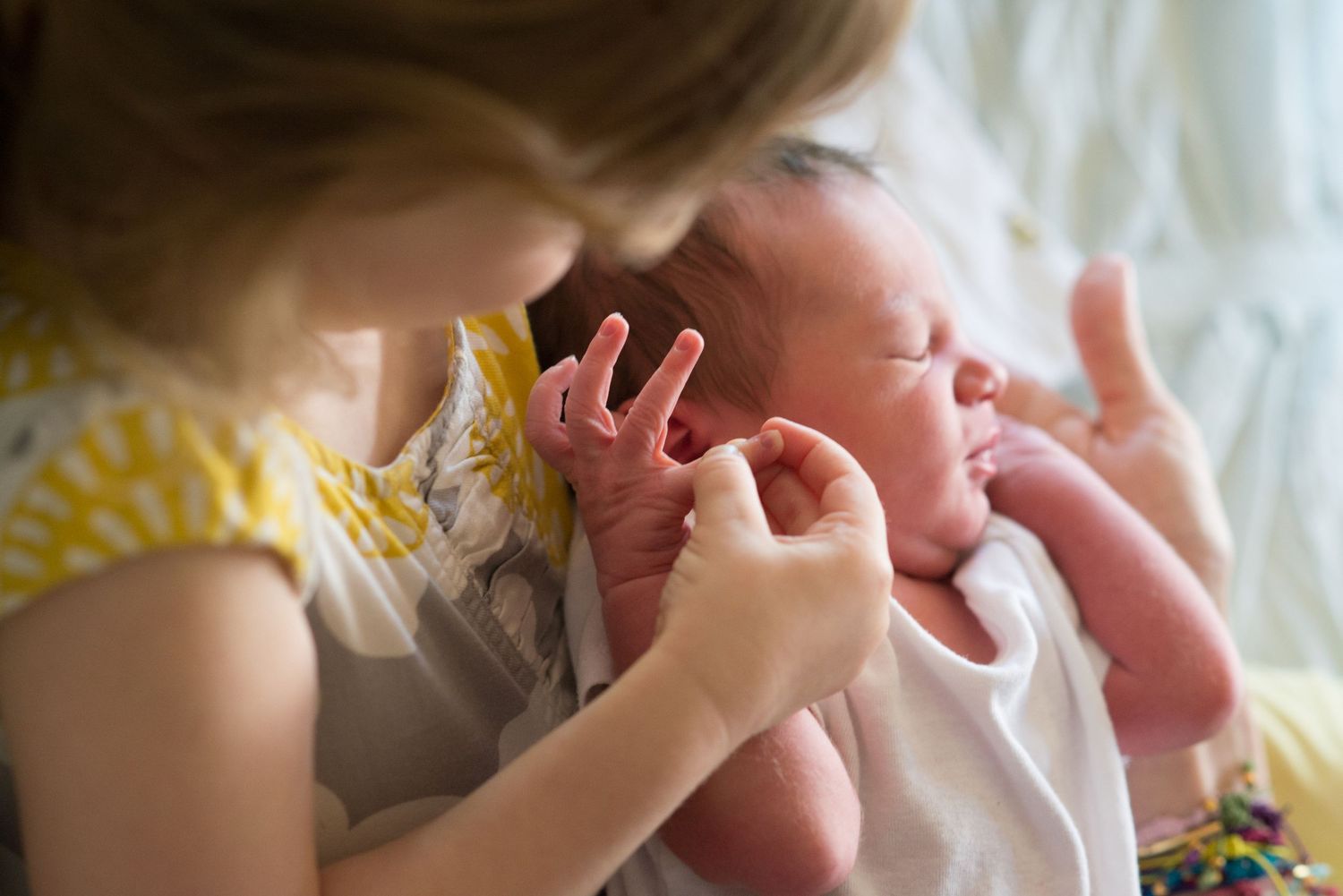 A small child gently touches and interacts with a newborn baby swaddled in white.