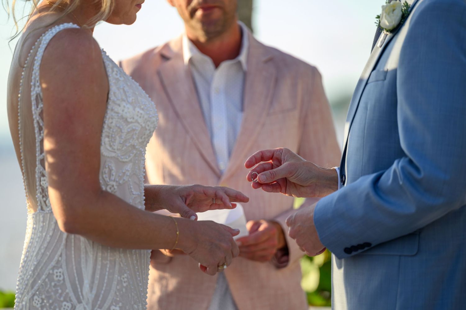 Close-up of wedding ring exchange ceremony with sunlight in background.