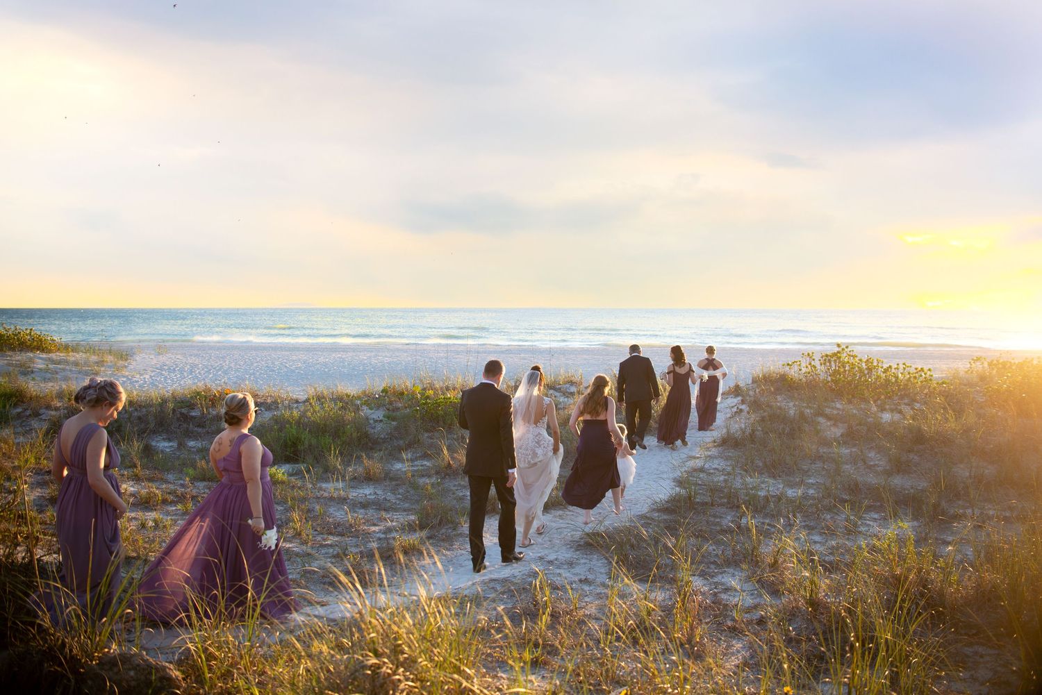 Group of people gathered on sandy beach dunes at sunset with golden light illuminating the coastal landscape.