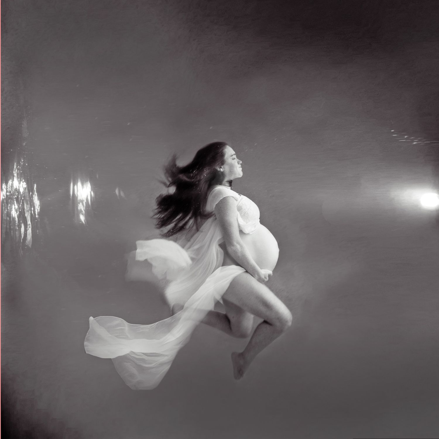 Ethereal underwater photography sequence showing a figure floating gracefully in dark water with flowing fabric.