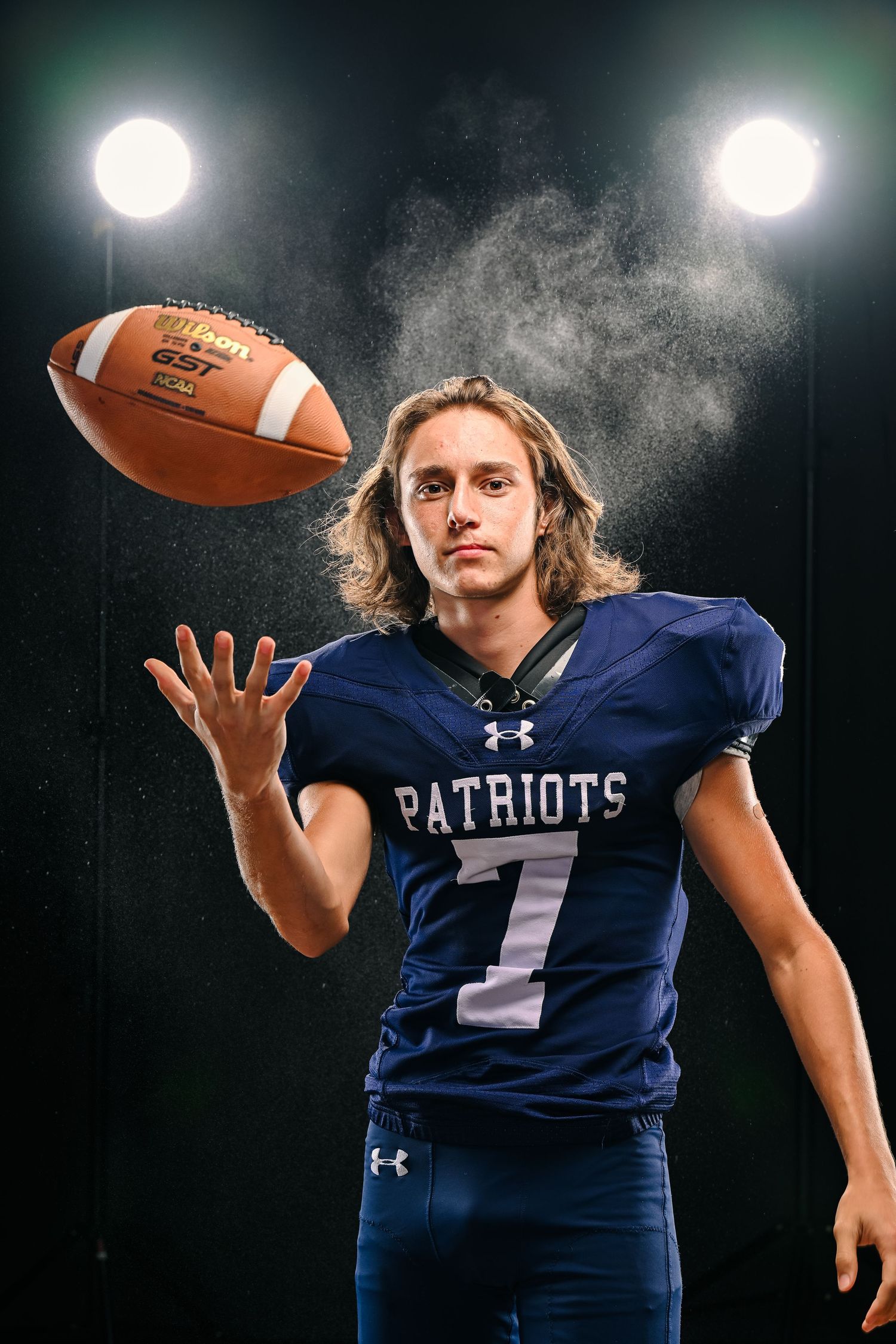 Football player in Patriots jersey demonstrates catching techniques under stadium lights.