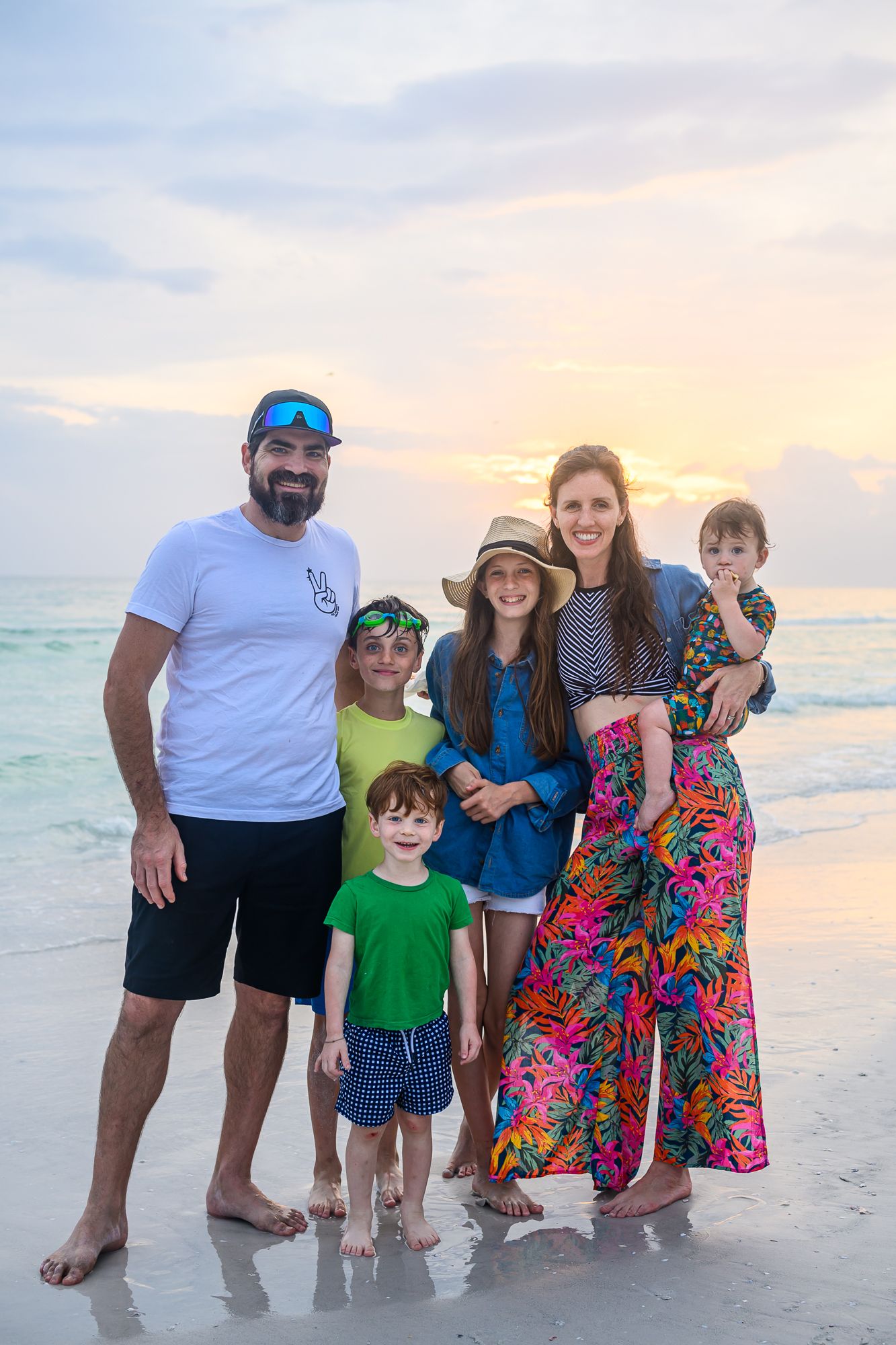Beach family portrait at sunset with colorful sky and ocean backdrop.