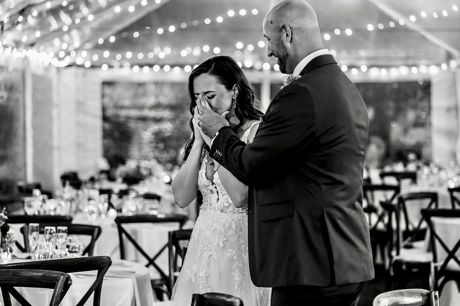 Emotional moment captured during first dance at outdoor wedding reception under twinkling lights.