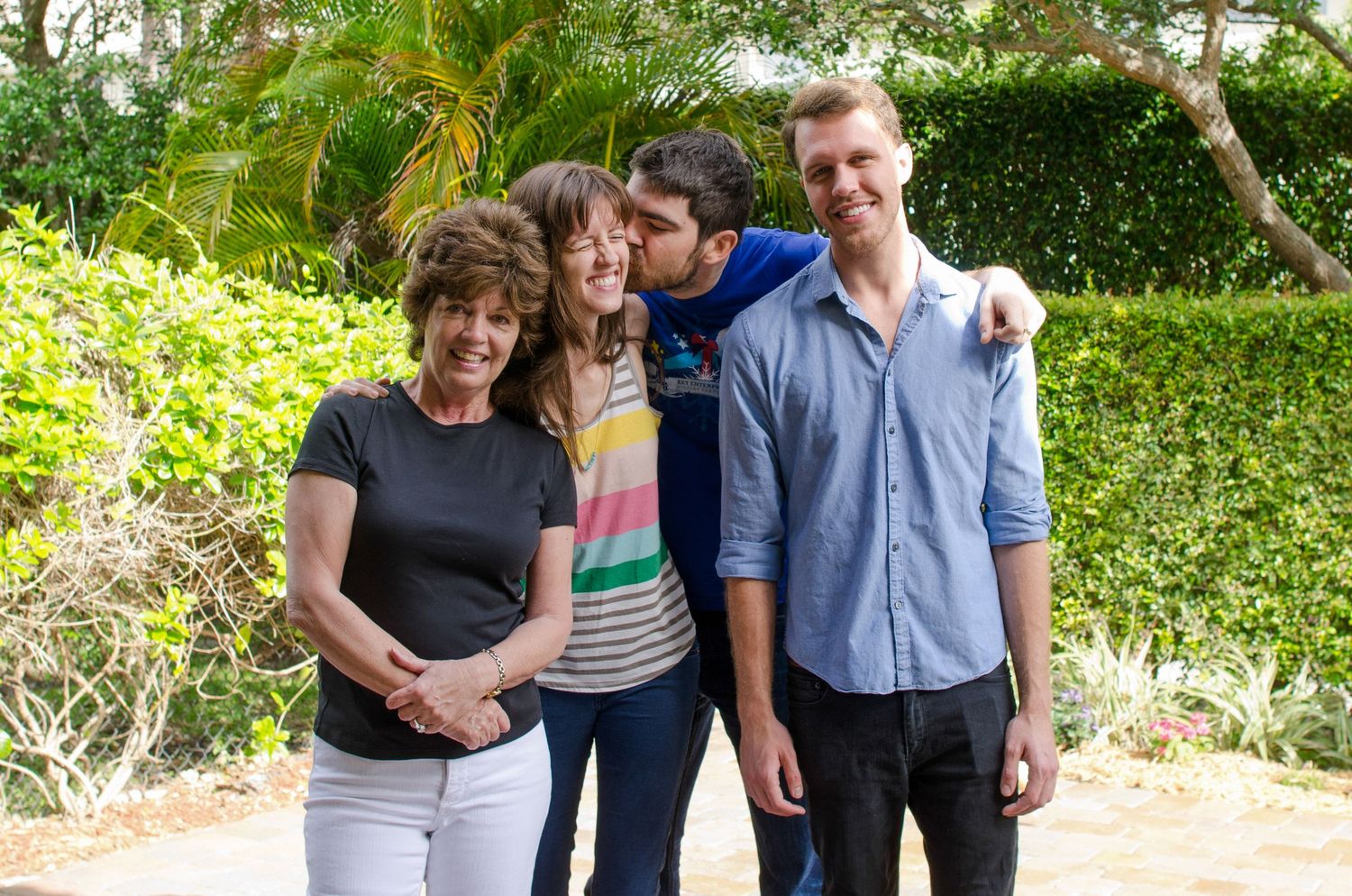 Family members posing together in a casual outdoor setting with green hedges in the background.