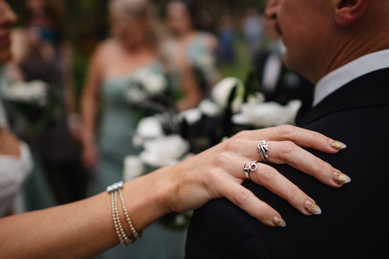 Close-up of bride's hand on groom's shoulder showing wedding ring set and gold nail polish.