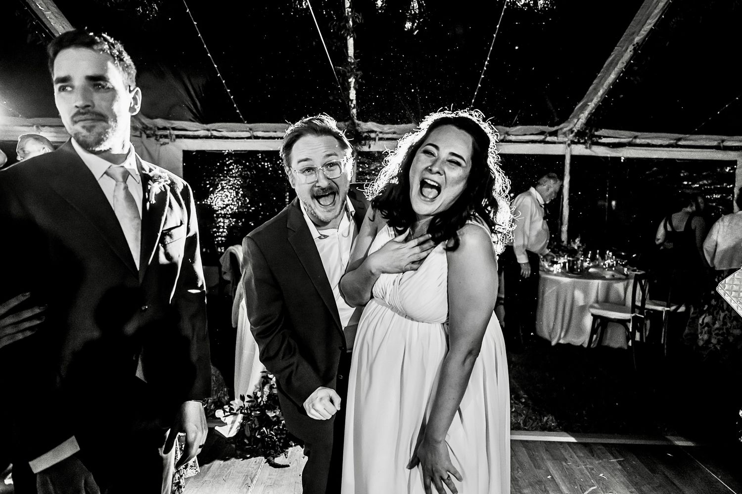 Wedding guests share a joyful candid moment dancing and laughing together during a celebration.