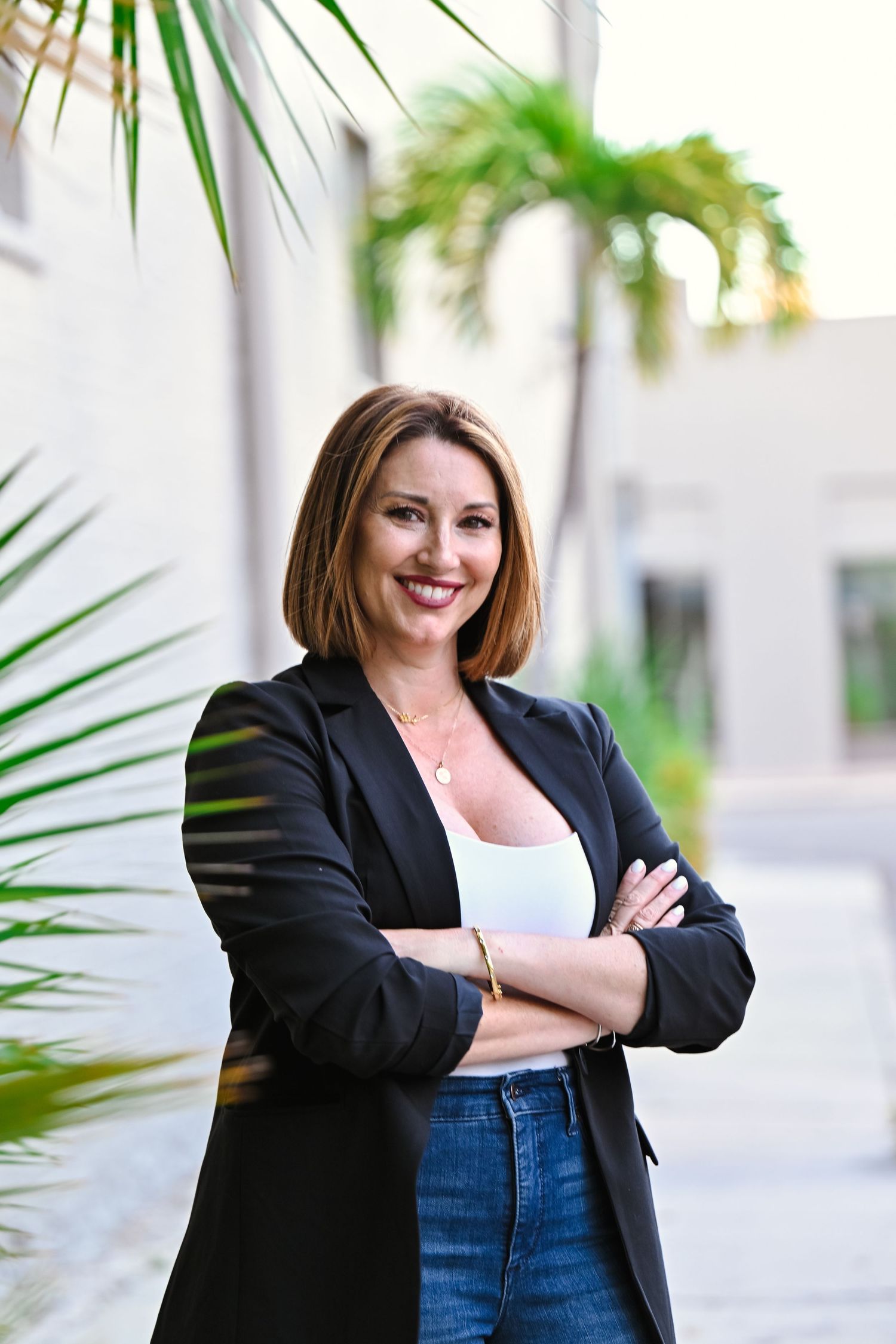 Professional wearing black blazer and jeans poses confidently against outdoor wall.