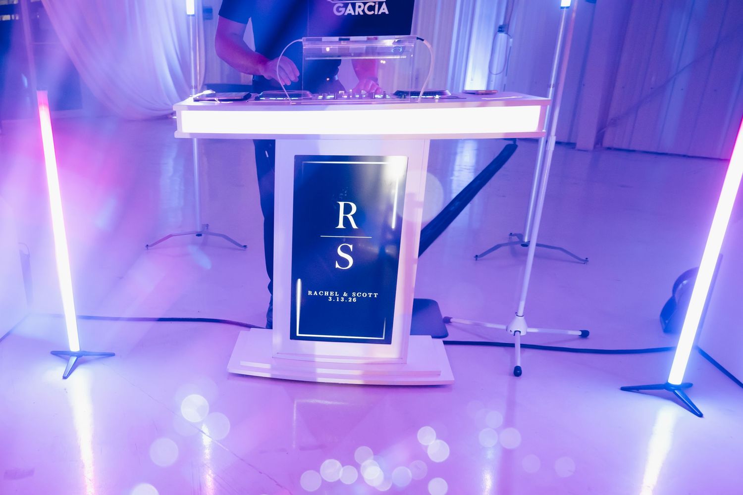 Elegant DJ booth with RS monogram display glowing in purple light at wedding reception.