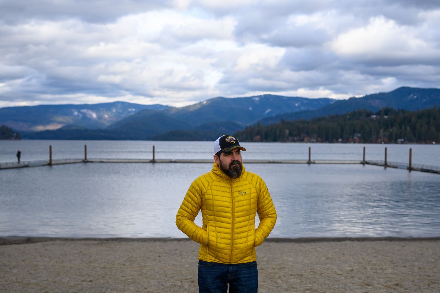 Person in yellow jacket standing by lake with mountain landscape in background.