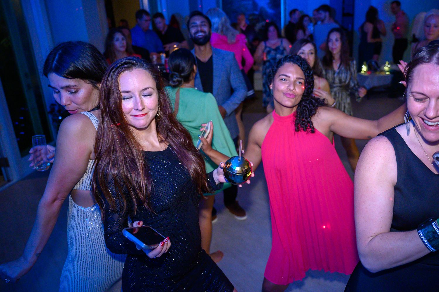 Energetic dancers move to music under blue and pink lighting at a party.