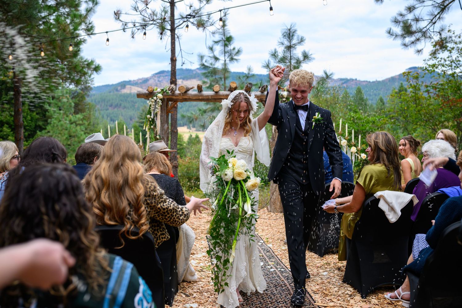 Bride and groom celebrate walking down the aisle at an outdoor forest wedding ceremony with mountain views.