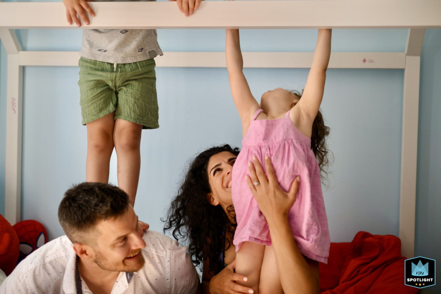 A joyful family moment with parents playing and lifting their child in a room with light blue walls.